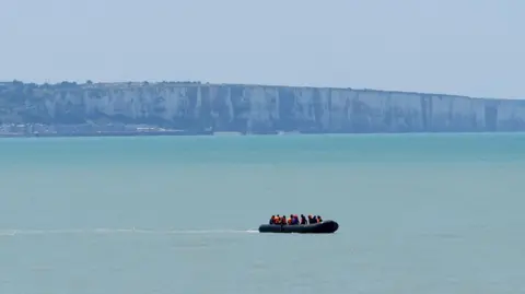 A small boat sails on a pale blue ocean.