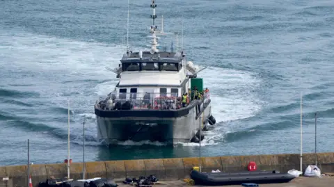 A large vessel with people in life jackets, arriving at a port. 