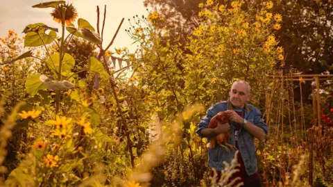 Jason Knott Photo of a man holding a large bird in a wood surrounded by flowers