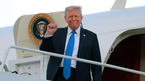 Trump, wearing a dark suit and light blue tie, holds up a fist while boarding Air Force One to visit Alabama on Thursday
