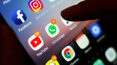 A mobile phone screen displaying several apps, with an index finger hovering over the WhatsApp icon.
