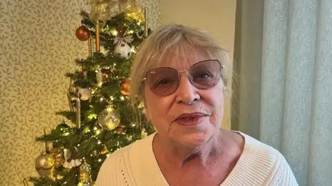 Penny Tooth stands in her front room next to a Christmas tree