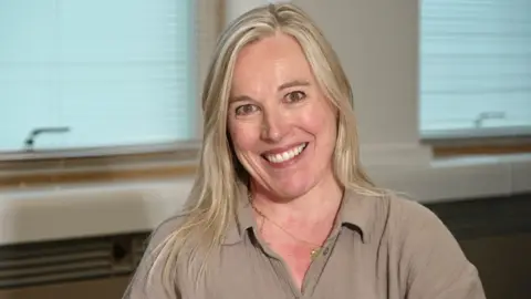 Mark Norman BBC A woman smiling at the camera. She has long blonde hair and is wearing a brown blouse.