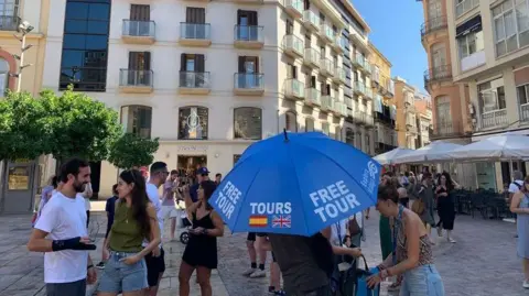 Guy Hedgecoe A circuit  guide, surrounded by tourists, holds an umbrella 