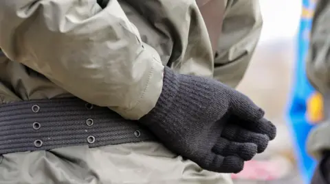 A hand behind the back of someone dressed in paramilitary uniform