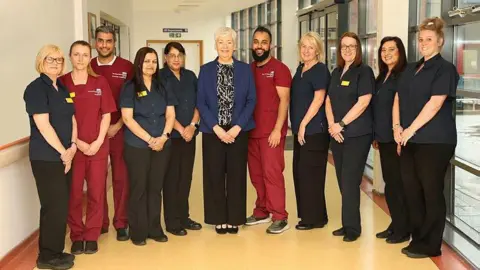 The Royal Wolverhampton NHS Trust Group shot of the ultrasound team at The Royal Wolverhampton NHS Trust. Eleven staff members are standing in a line in a hospital building. 