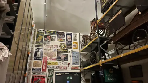 Shelves on the right hand side contain model wagons while a wall at the back is covered in multi-coloured advertising signs.