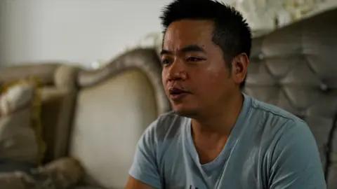 Chinese man wearing a blue t shirt sitting on a couch