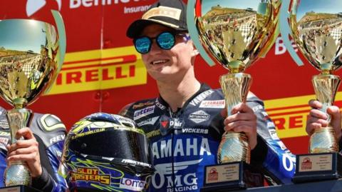 Ryan Vickers wearing sunglasses lifts a trophy on the winner's podium
