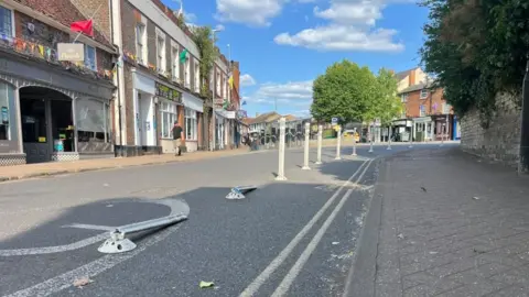 Holly Nichols/BBC A road in Leighton Buzzard, showing several bollards, two on the ground, with shops in the distance, a path and a road.