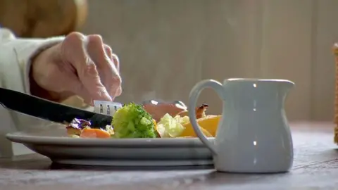 BBC A close-up of a plate of food while somebody is eating. A white milk jug is placed on the table next to the plate.