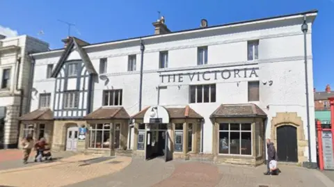 Google Street view of a large three storey pub with stone window surrounds and white render. The words "The Victoria" are written in large black letters on the wall.