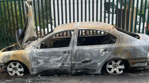 West Midlands Police A burnt car abandoned in front of a gate