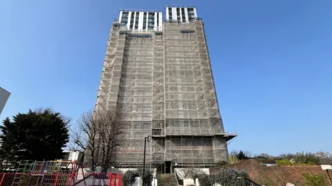 BBC/Harry Low Dorney House Tower Block ditutupi terpal kecuali empat lantai atas di atas langit biru