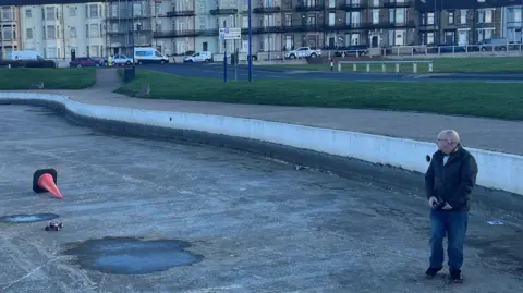 A club member racing a radio controlled car in the empty lake. There is an overturned orange cone.