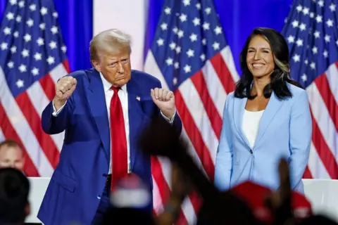 Getty Images Donald Trump dancing on stage with his defence chief Tulsi Gabbard smiling. Both have US flags behind them