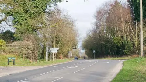 An eastbound view along Mortimers Lane, showing Knowle Lane on the right. The single carriageway has an additional turning lane at the junction.
