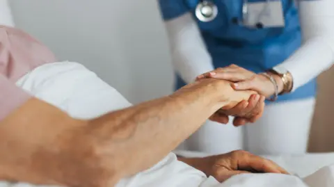 Close-up of caregiver holding senior client hand. Support from nurse to patient, taking care of elderly man in hospital. Stock photo