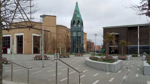 Owen Ward/BBC A view of St Martin's Square in Basildon, showing the large, cream brick council offices and glass bell tower. There are benches and planters dotted around the grey square.