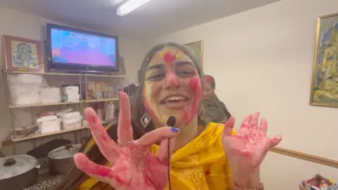 Girl dressed in orange with coloured powder on her hands and face