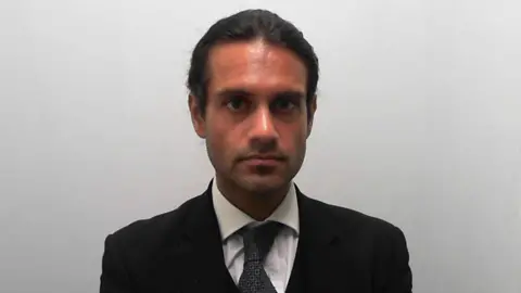 Custody picture of a man with tied up dark hair, wearing a three-piece suit