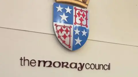 'The Moray Council' on a wall under a red, white and blue coat of arms.