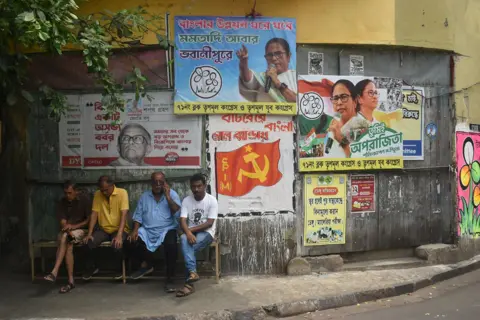 Sudipta Das / NurPhoto via Getty Images A group of people sit on a bench next to political party campaign posters on a wall on a street in Kolkata on 29 March