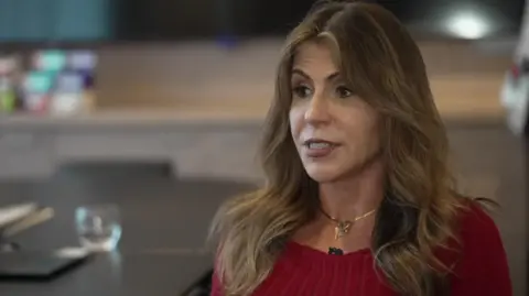 Ella Rauen-Prestes, who is wearing a red jumper and has long brown hair, is sitting at a table in an office setting