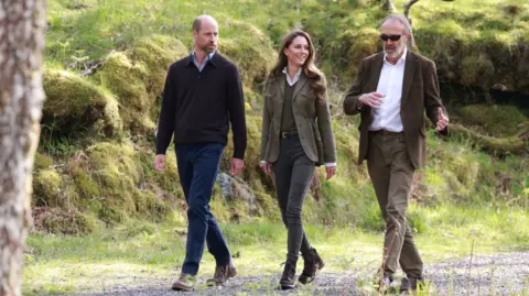 Reuters William and Catherine are guided through the forest by a man with grey hair, wearing sunglasses, a green jacket and trousers and a white shirt