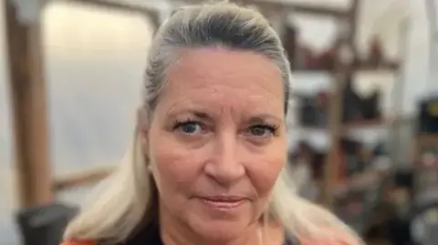 Penny is standing in a gardening shed at the Kenward Trust site in Yalding near Maidstone. She has long blonde hair.