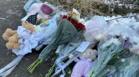 Bunches of flowers and two teddies lie on a woodland path.