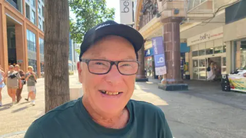 Zac Sherratt/BBC Bob Killminster pictured in Redhill. Bob is wearing a green t-shirt, cap and glasses. 
