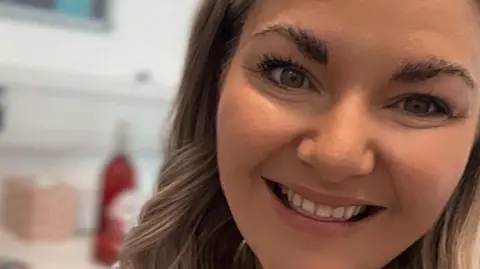 A selfie of Siobhan Gorman who has long wavy blonde hair and is smiling. She is in an office.