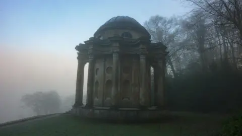 Stourhead - National Trust A foggy building which is rounded and has Roman-style pillars leading to its rounded roof.