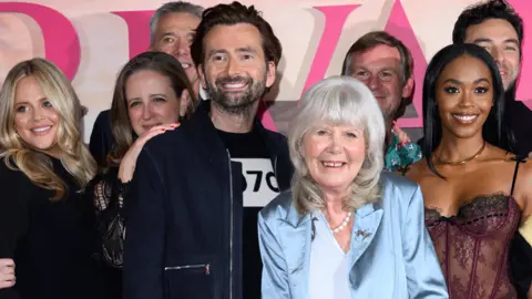 Getty Images Dame Jilly Cooper is wearing a blue satin suit and stands alongside actors including David Tennant in a group picture. She is smiling at the camera and has her grey hair lose with a fringe. 