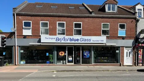 The shopfront of Bristol Blue Glass. A red brick building with glass windows in stretching the width of the building. 
