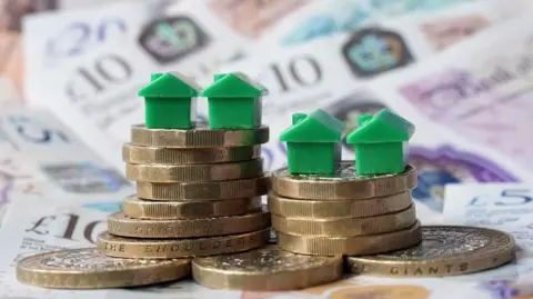 PA Media Bank notes and coins with green plastic houses balanced on top
