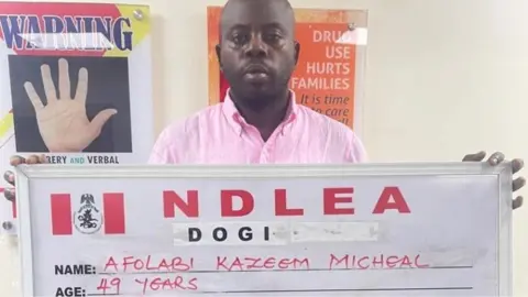 Afolabi Kazeem Micheal holds up a NDLEA sign with his name and age after his arrest in Lagos