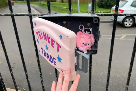 A hand opening a pink trinket trade box with a small pink soft toy inside