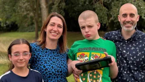Contributed The Saul family stand together outside. Mother Sarah stands with her daughter Amelia on the left and son William to the right. Father Gareth stands on the end on the right. They are smiling at the camera. Williams holds a gaming device in his hands. 
