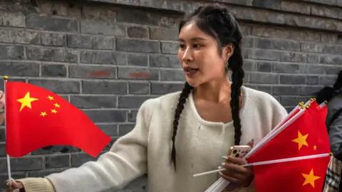 Getty Images Uma mulher vende bandeiras chinesas em um bairro histórico de Pequim antes das comemorações do Dia Nacional.