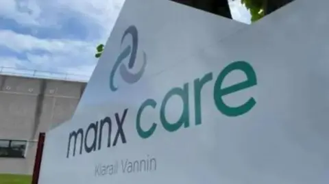 A large white Manx Care sign, which has MANX CARE written on it in grey and green, with the healthcare provider's logo above it.