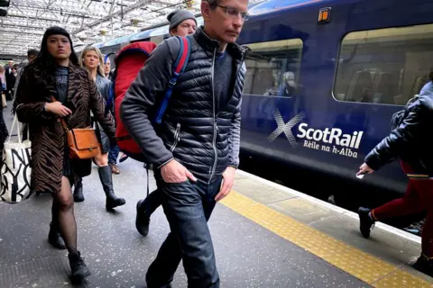 PA Media People walk on the platform at Glasgow Central by a ScotRail train