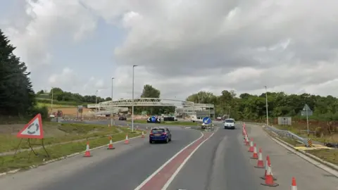  The Landkey Junction on the A361 it shows a roundabout and traffic moving in both directions. The road is lined with traffic cones. 