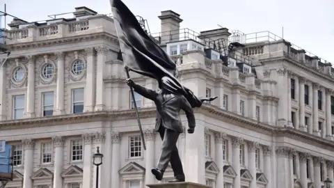 Getty Images A grey statue of a man wearing a suit, walking forward, carrying a flag that covers his face
