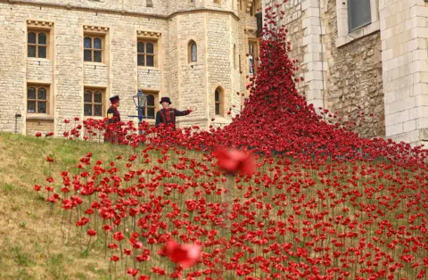 Getty Images A sea of red ceramic poppies flow down from the wall of the Tower of London onto the grass outside the building, with guards in uniform in the background.
