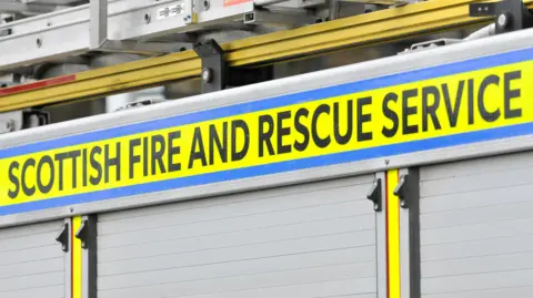 Getty Images A close up of the side of a fire engine. There are ladders on the roof of the vehicle with the words "Scottish Fire and Rescue Service" written on it in black letters on a yellow background.