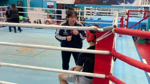 UK Coaching Suzanne wearing a black tracksuit top and is giving instructions to a young fighter.