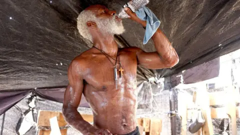 A man drinks water while cooling down in his tent in Phoenix's largest homeless encampment, amid the city's worst heat wave on record on 25 July , 2023