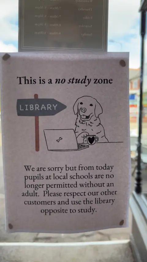 Tom Griffin A sign stuck to a window. It reads - "This is a no study zone. We are sorry but from today pupils at local schools are no longer permitted without an adult. Please respect our other customers and use the library opposite to study." The picture to accompany the message is a dog with a coffee in front of a laptop with a narrow sign pointing to "library".